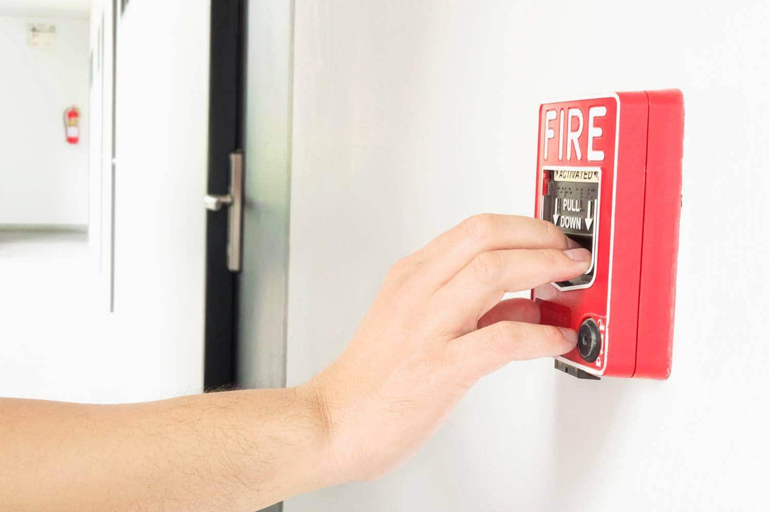 Mana care activeaza un buton rosu de alarma de incendiu pe un perete alb