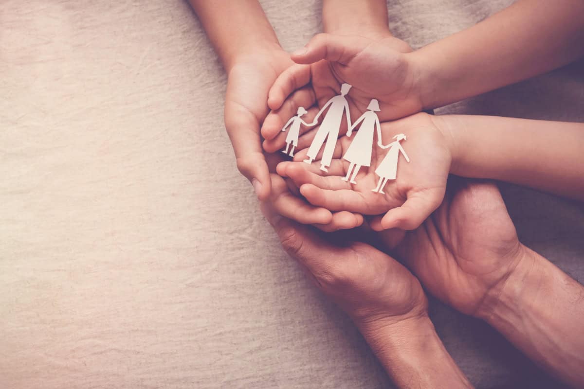 Mai multe maini de adulti si copii tin un decupaj din hartie reprezentand o familie