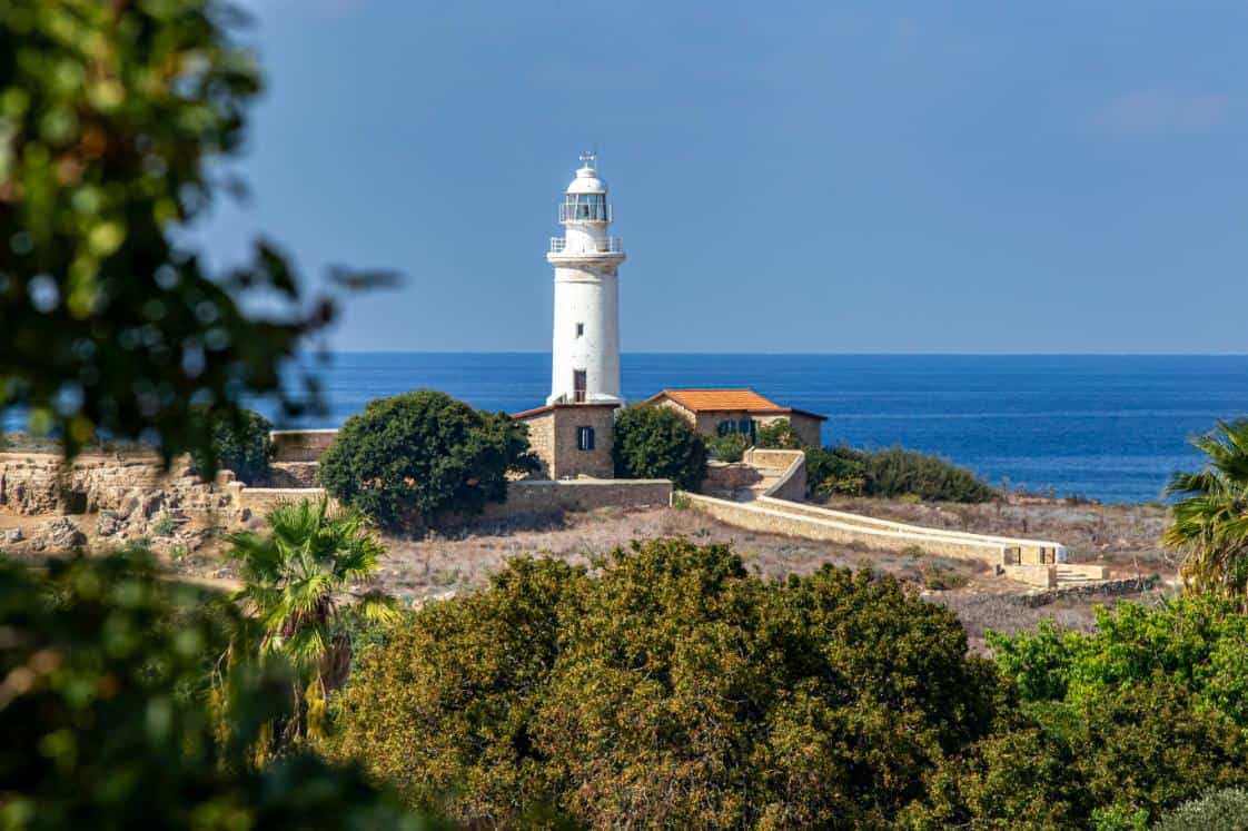 Far alb langa mare inconjurat de cladiri joase si vegetatie mediteraneana