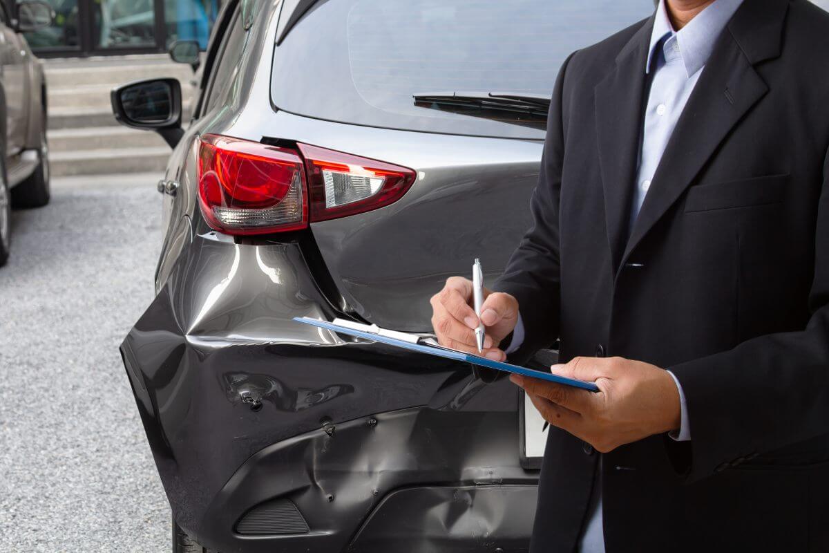 Inspector auto care noteaza detalii pe o fisa in fata unei masini aviariate pe partea din spate