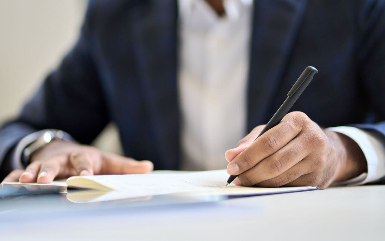 O persoana imbracata in costum scrie intr-un document oficial