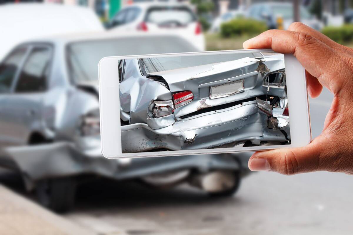Sofer care fotografiaza cu telefonul o masina gri avariata pe partea din spate