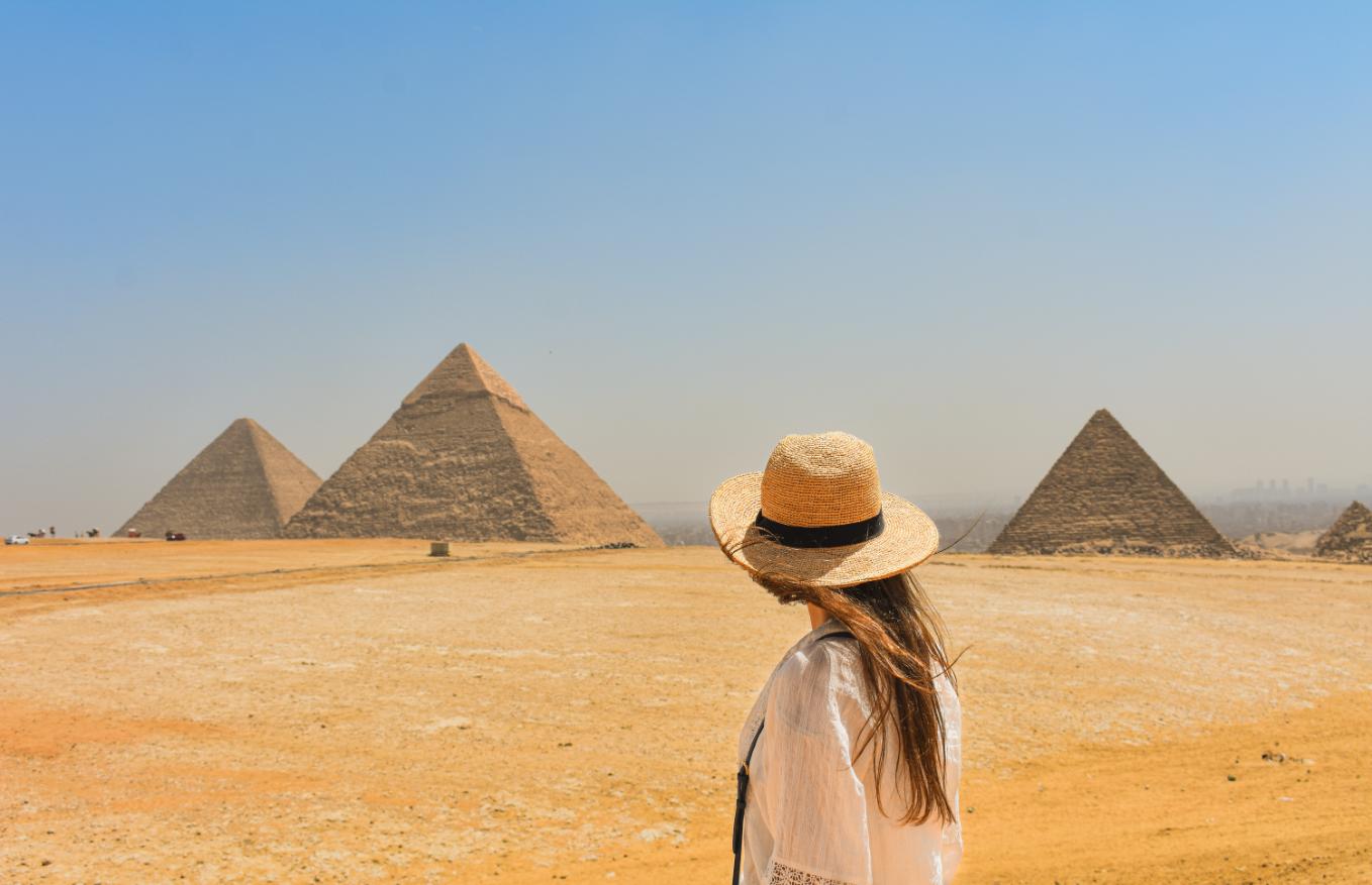 Femeie cu palarie in desert privind spre piramidele din egipt