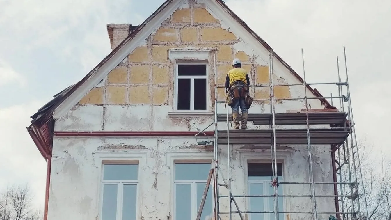 Muncitor pe schelă lucrând la renovarea fațadei unei case