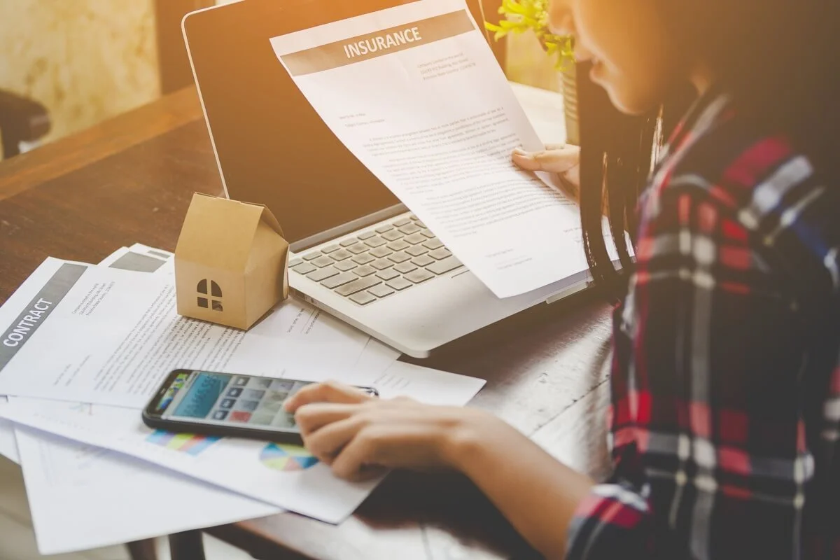 Femeie care cerceteaza asigurarea PAD cu laptop, macheta de casa si documente pe masa