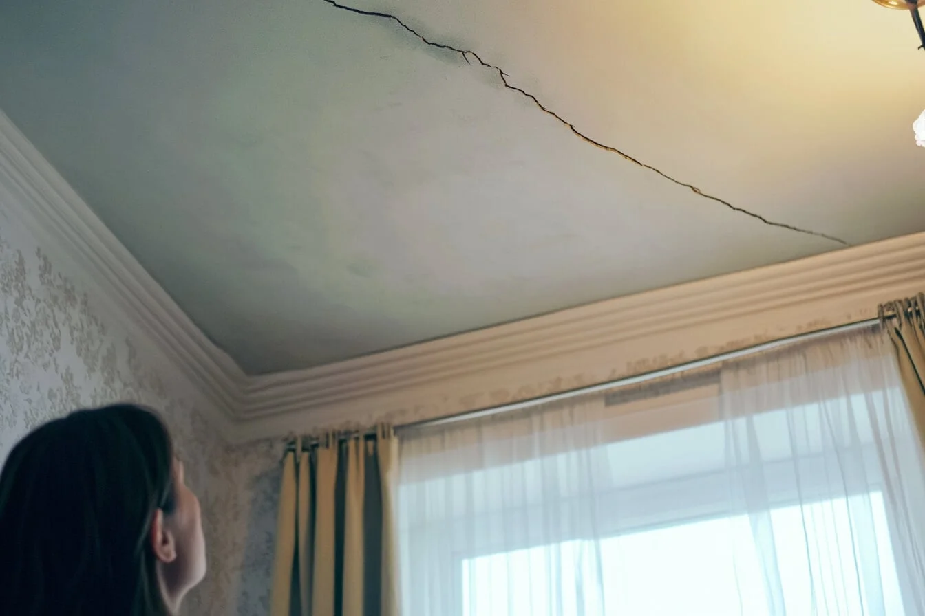 Femeie privind o fisură adâncă pe tavanul unui apartament vechi