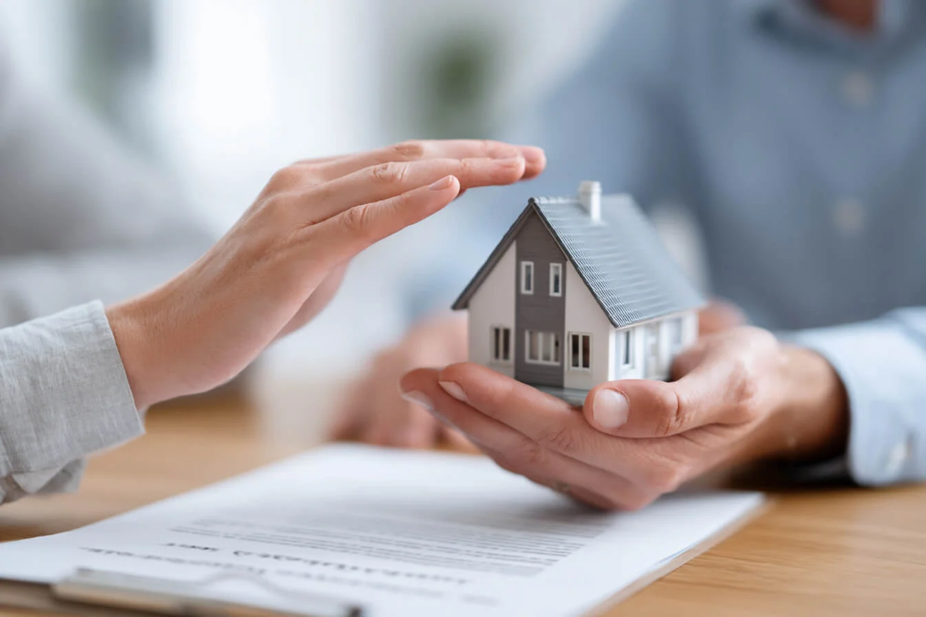 Doua maini tin o macheta de casa deasupra unei polite de asigurare